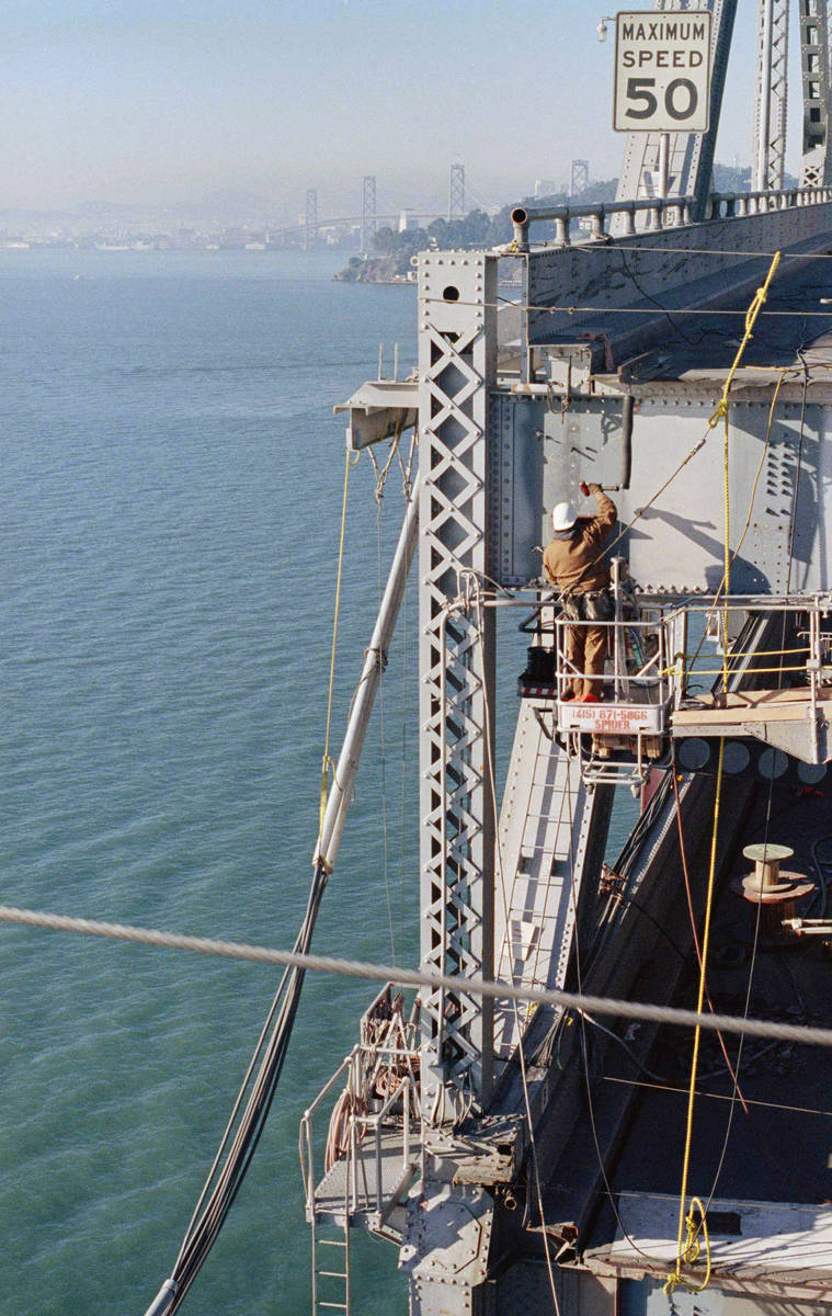 A bridge worker checks bolt hole alignment and readies to attach a support fro I-beams that wil ...