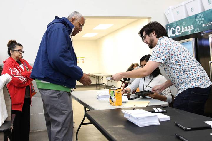 Nation Graca, right, site leader, hands out voting card to Reginald Bates of Las Vegas during t ...