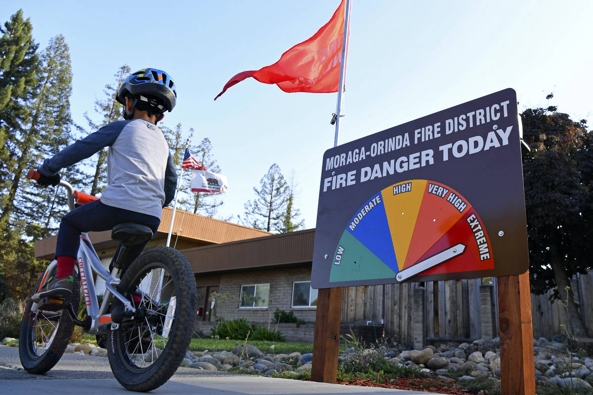 A boy rides his bike past the fire danger meter showing extreme fire danger in front of the Mor ...