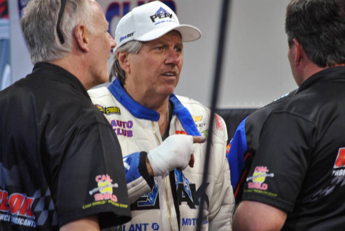 John Force talks to crew members after his Funny Car blew an engine and destroyed the body of h ...