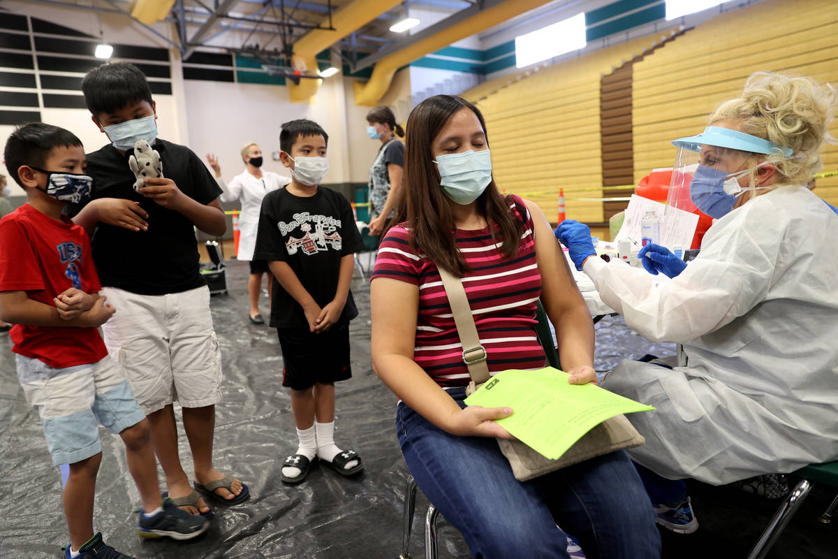 Melanie Navarrete of Las Vegas gets a flu vaccine from Lynda McCloskey as her children, from le ...