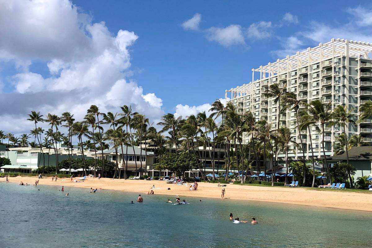 People are seen on the beach and in the water in front of the Kahala Hotel & Resort in Honolulu ...