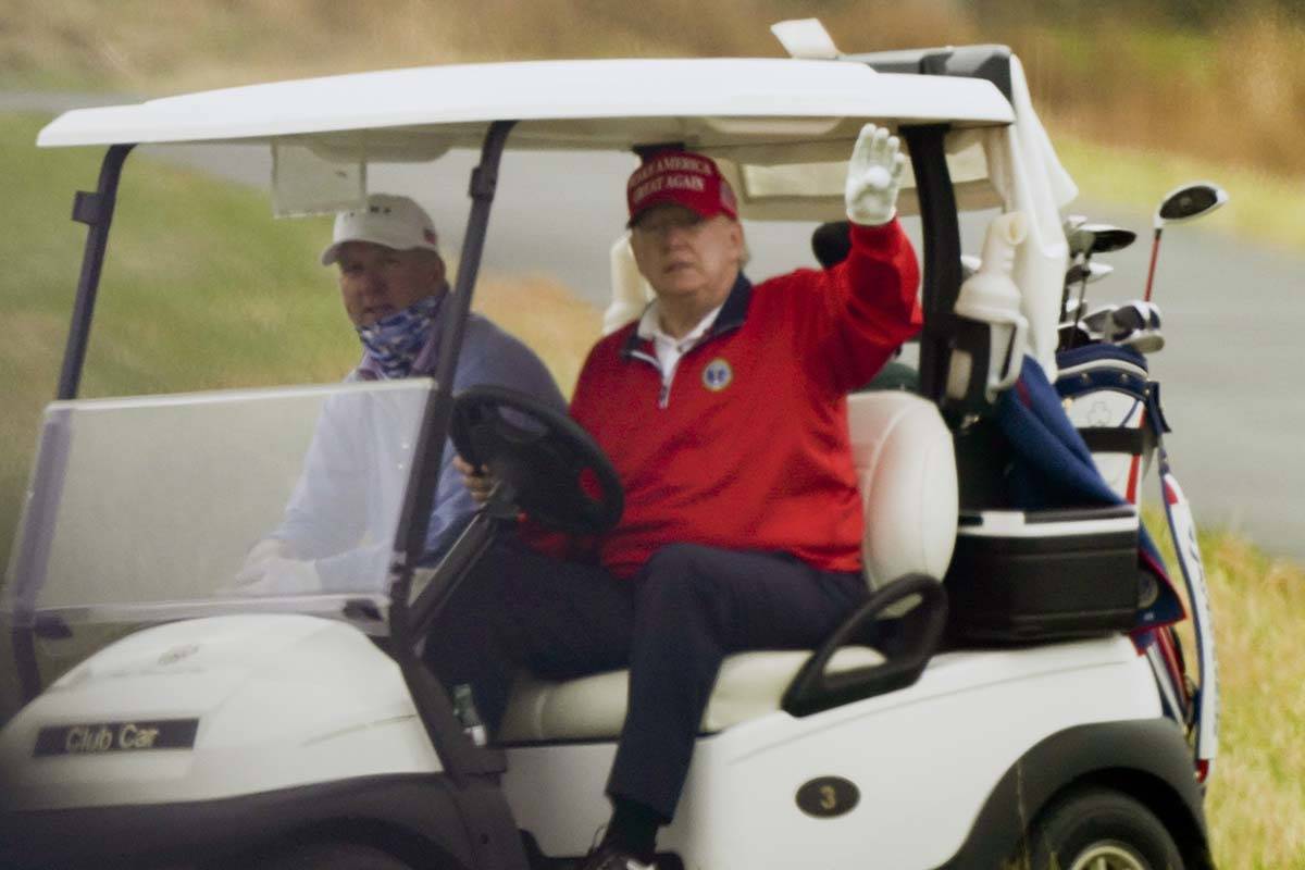 President Donald Trump waves from a golf cart as he plays golf at Trump National Golf Club, Fri ...