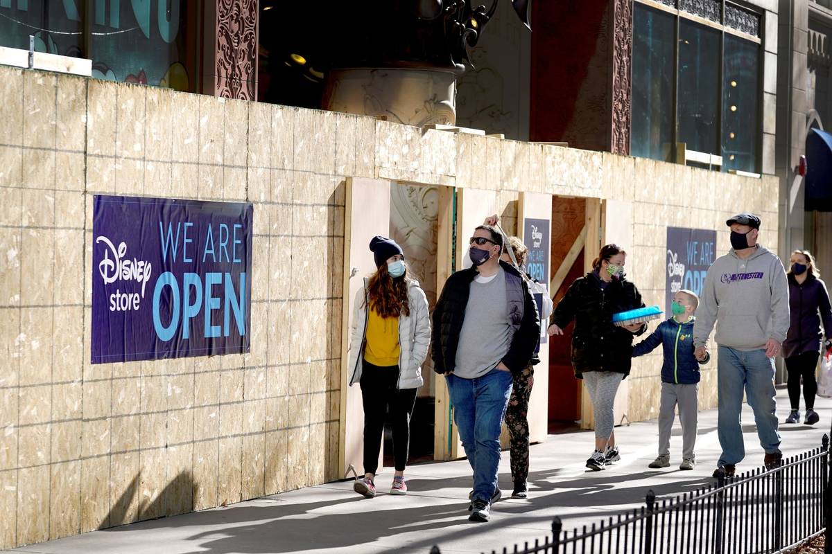 Shoppers pass Saturday, Nov. 28, 2020, an open Disney Store that is still partially boarded up ...