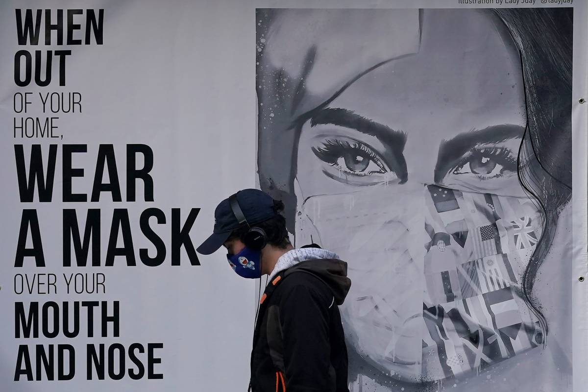 A pedestrian walks past a mural reading: "When out of your home, Wear a mask over your mouth an ...