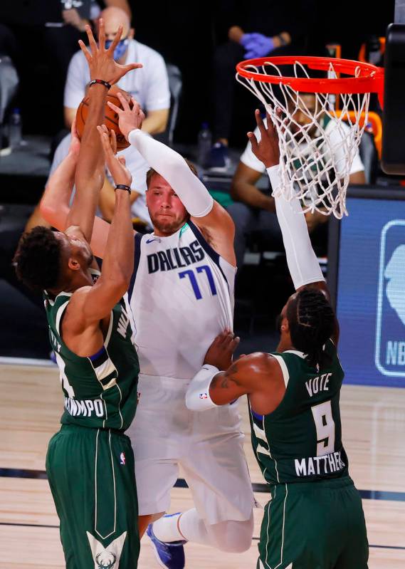 Dallas Mavericks' Luka Doncic (77) passes around Milwaukee Bucks' Giannis Antetokounmpo (34) an ...