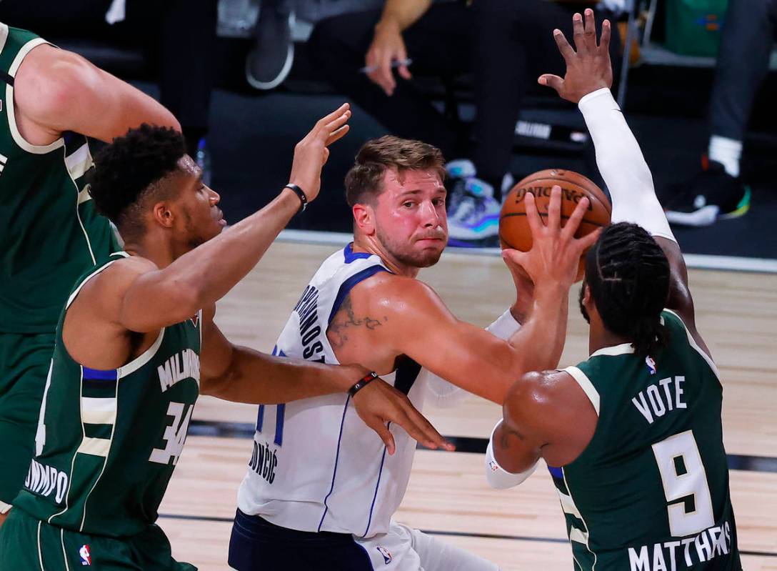 Dallas Mavericks' Luka Doncic, center, looks to pass the ball as Milwaukee Bucks' Giannis Antet ...