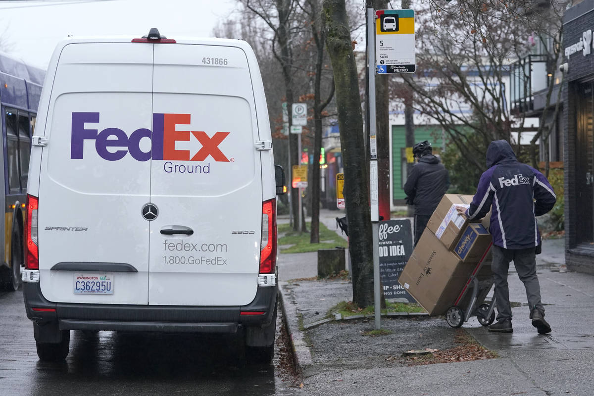 A driver with FedEx carries a package away from a van, Tuesday, Dec. 8, 2020, in Seattle. Store ...