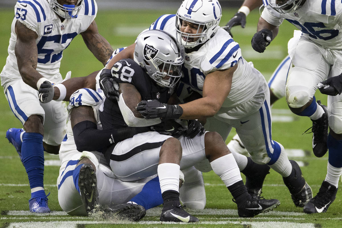 Raiders running back Josh Jacobs (28) is stacked up by Indianapolis Colts outside linebacker Da ...