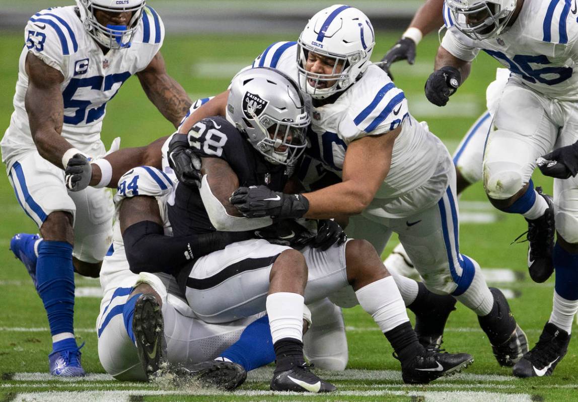 Raiders running back Josh Jacobs (28) is stacked up by Indianapolis Colts outside linebacker Da ...