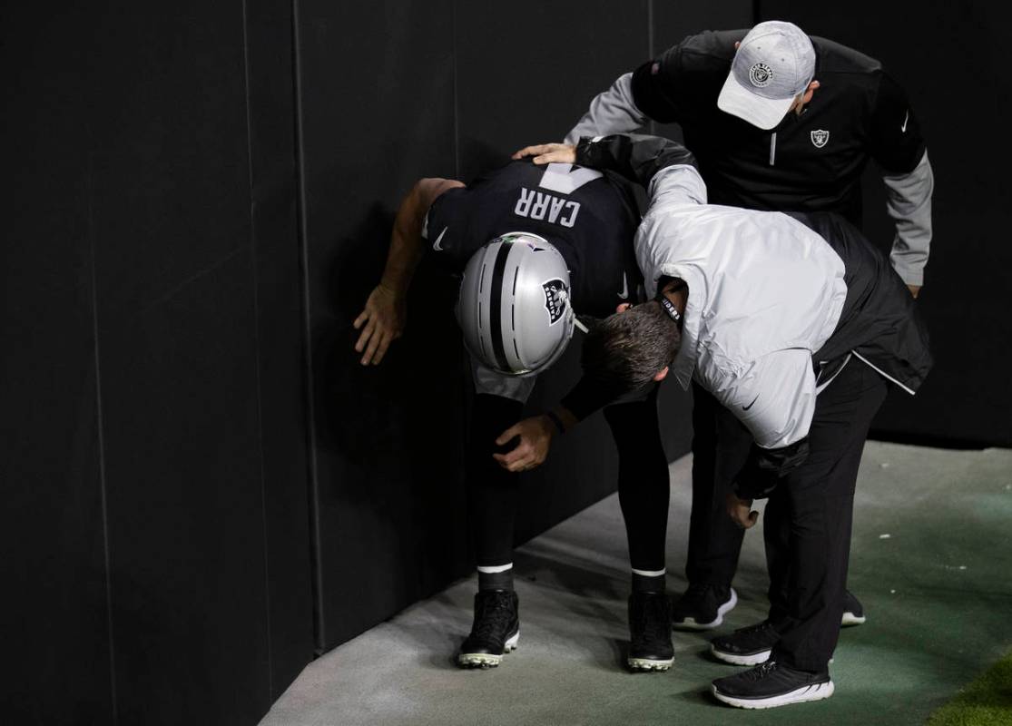 Raiders quarterback Derek Carr (4) hunches over while talking to training staff after getting h ...