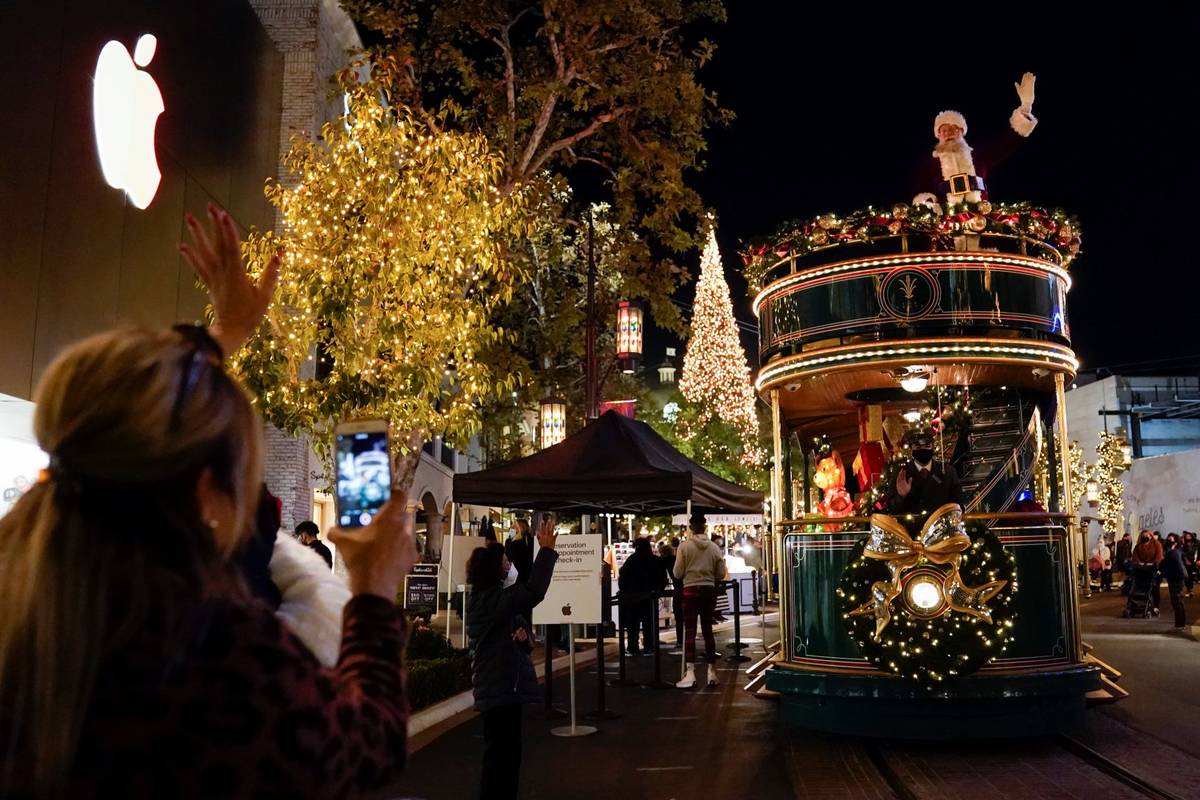 Santa Claus waves to shoppers from a safe distance at the top level of a trolly at The Grove sh ...