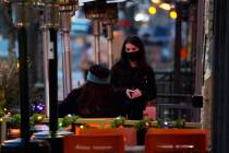 A waitperson wears a face mask while tending to a patron sitting in the outdoor patio of a sush ...