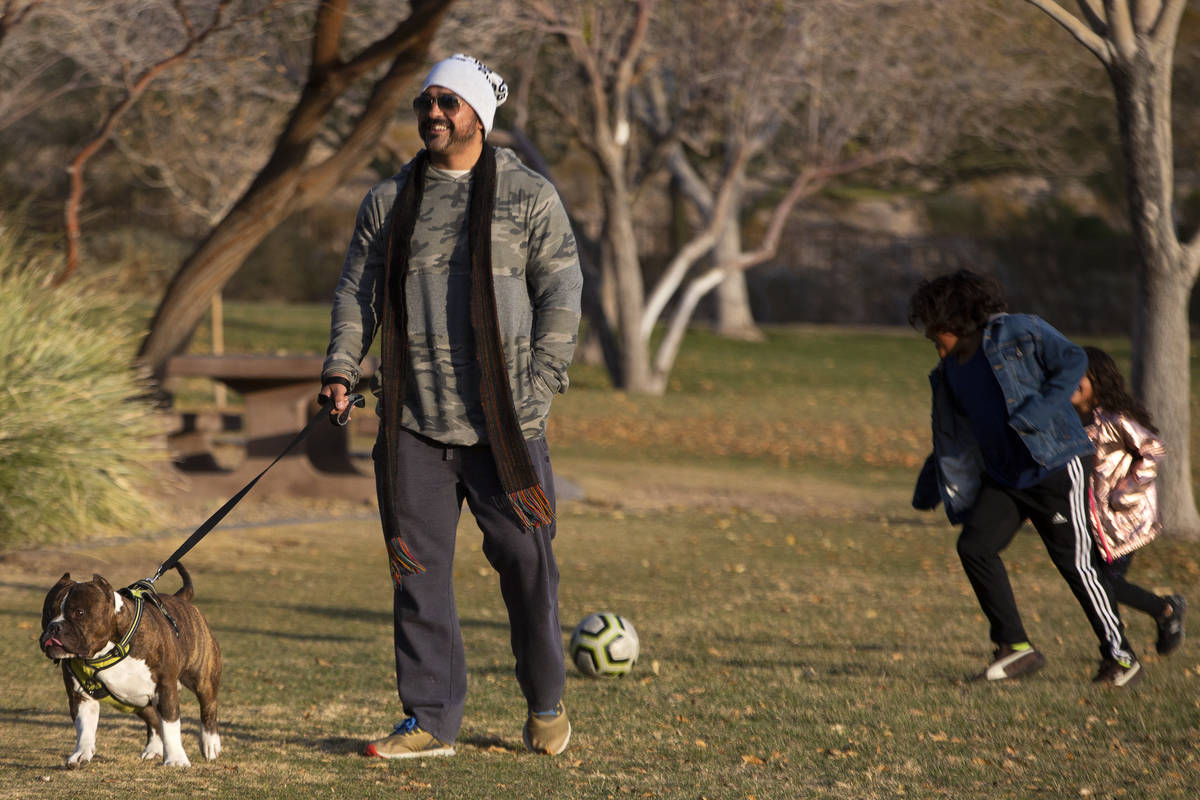 Orlando Farias walks his dog, Freddie, while his children play soccer in the background at Expl ...