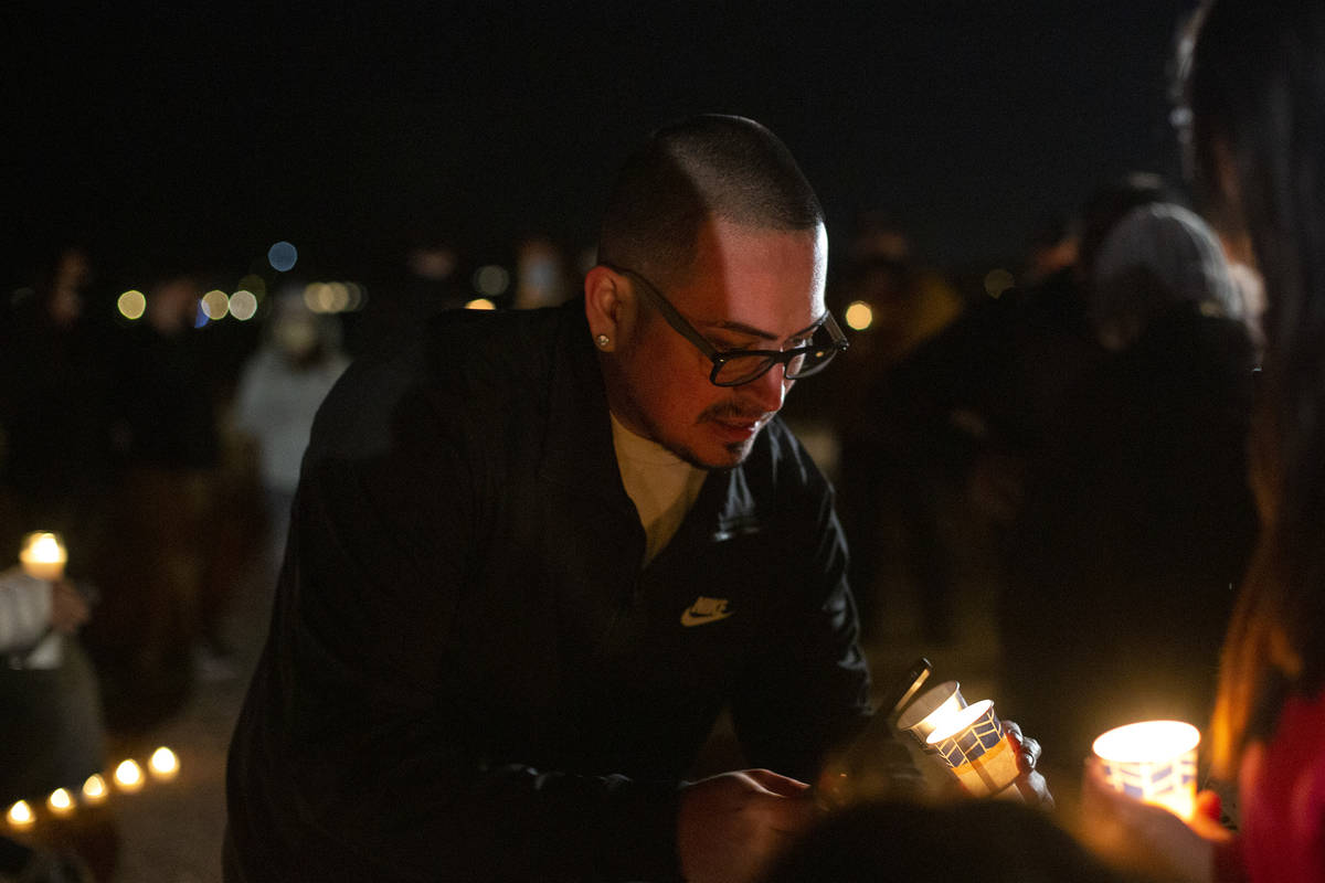 Christopher Meneses, nephew of Eric Echevarria, helps light candles during a vigil for his uncl ...