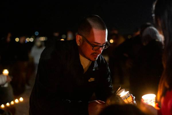 Christopher Meneses, nephew of Eric Echevarria, helps light candles during a vigil for his uncl ...