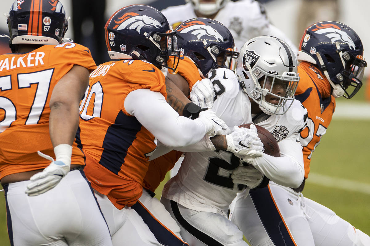 Raiders running back Josh Jacobs (28) drives forward with a group of Denver Broncos on his back ...