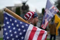 A man carries a U.S. flag attached to a baseball bat as he waits at the Capitol in Olympia, Was ...