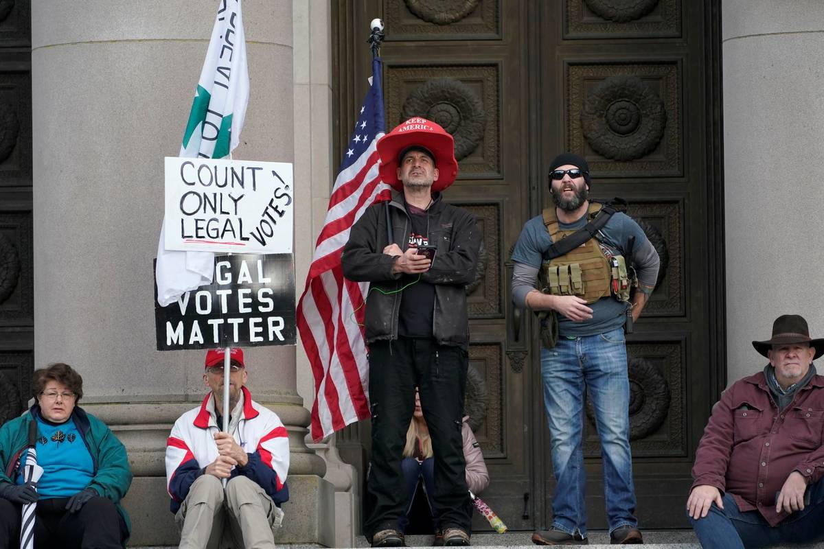 People hold signs and flags as they stand on the steps of the Temple of Justice at the Capitol ...