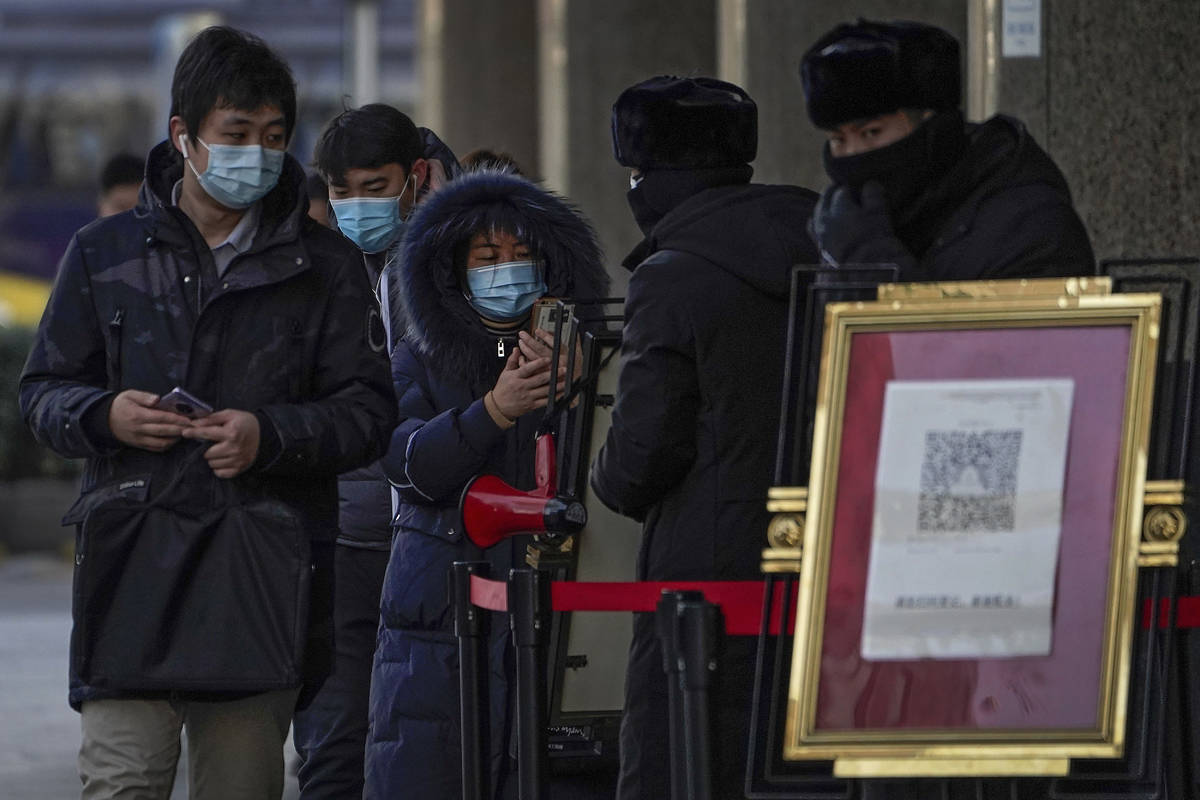 People wearing face masks to help curb the spread of the coronavirus use smartphones to scan th ...