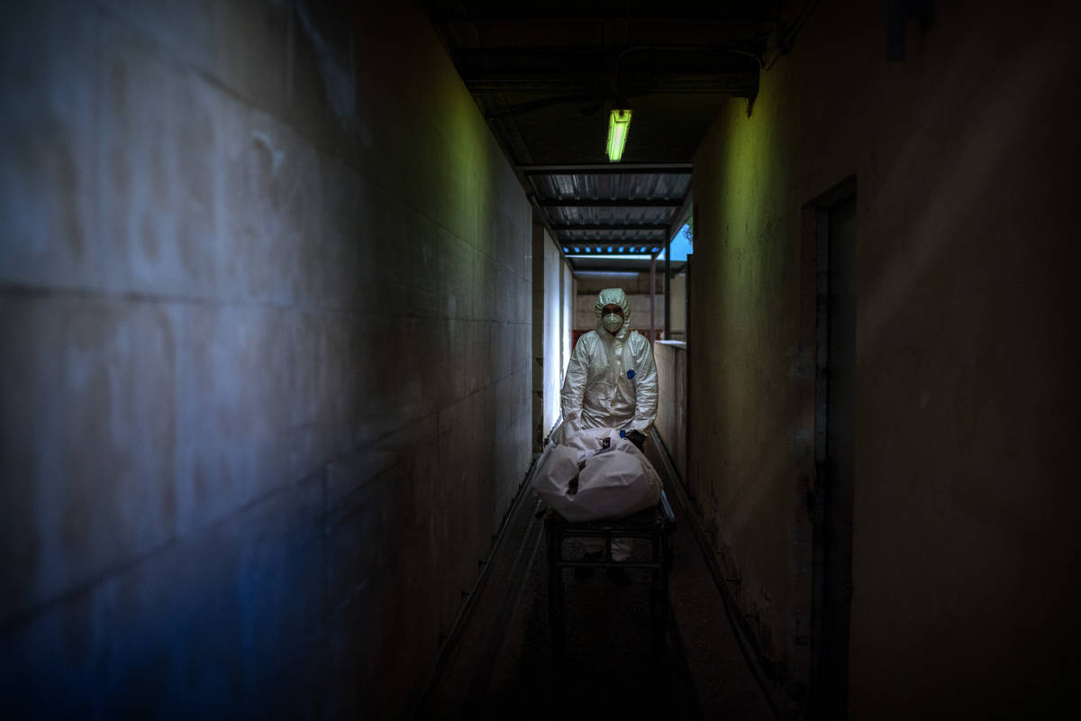 A mortuary worker transports the body of a COVID-19 victim on a stretcher at the morgue of a ho ...