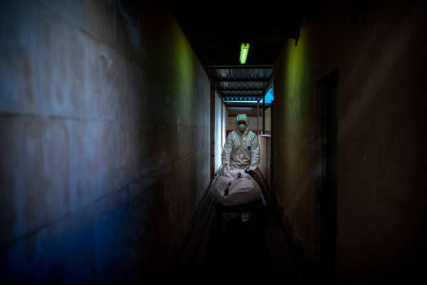 A mortuary worker transports the body of a COVID-19 victim on a stretcher at the morgue of a ho ...