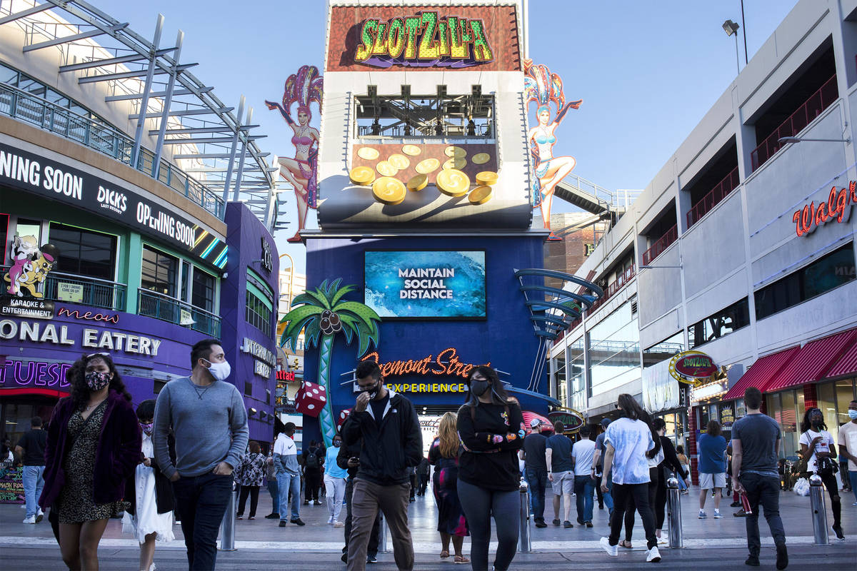 Pedestrians, masked to prevent the spread of coronavirus, roam Fremont Street Experience while ...