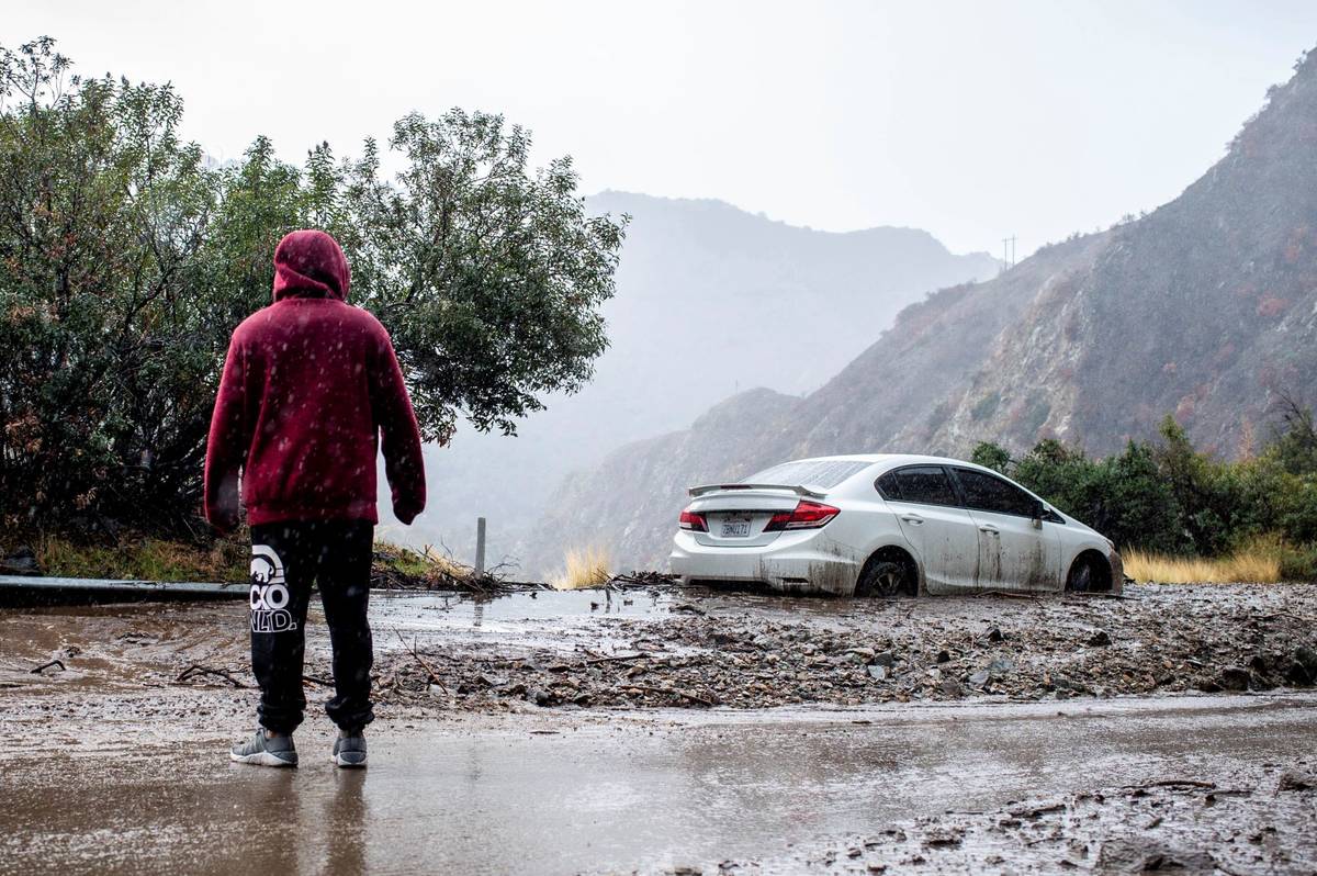 A man waits for Caltrans to clear a mudslide where a vehicle was trapped on Highway 39 in the S ...
