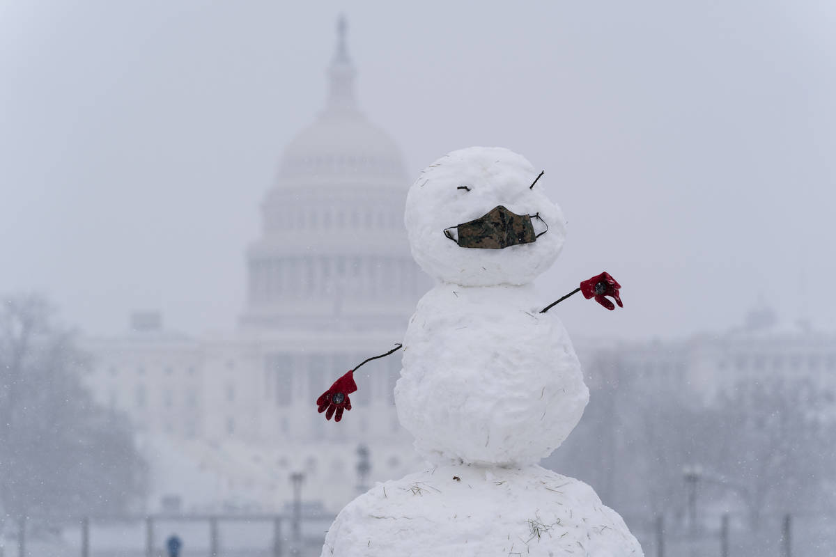 A snowman on the National Mall wears a face mask as snow falls in front of the U.S. Capitol, Su ...