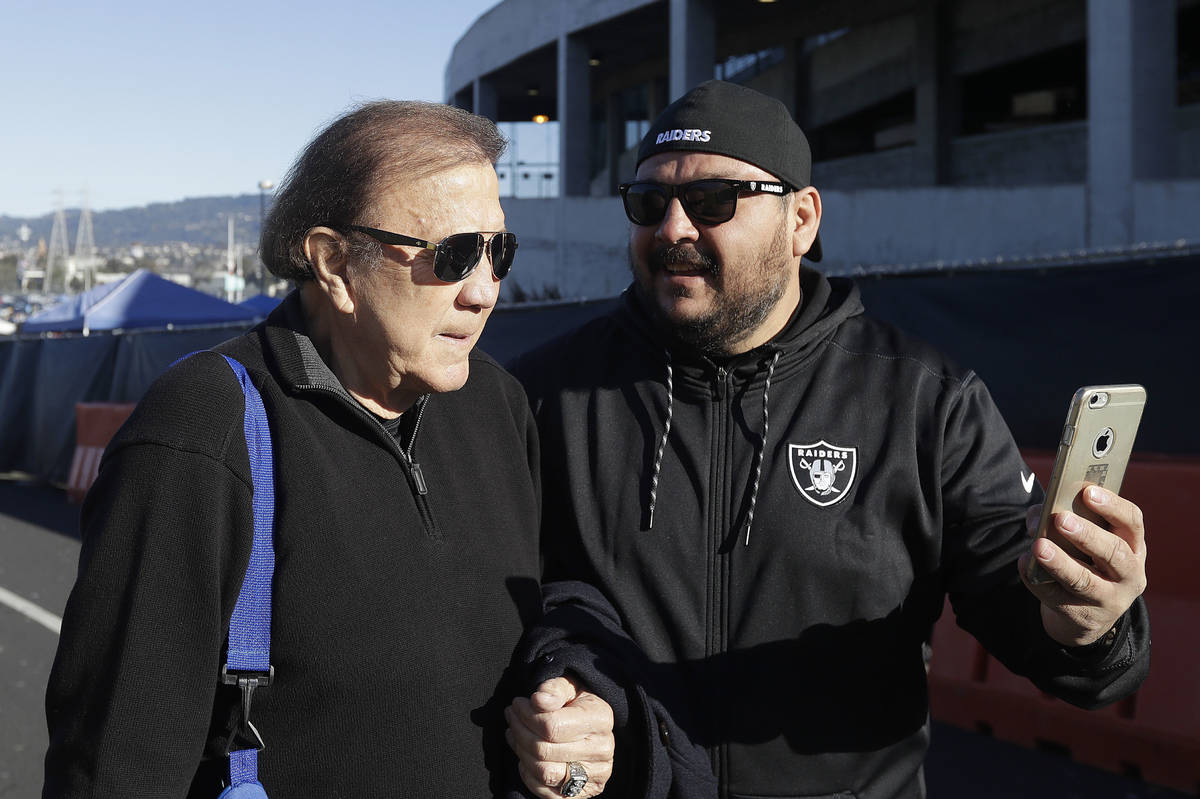 Former Oakland Raiders head coach Tom Flores, left, takes a photo with a fan before an NFL foot ...