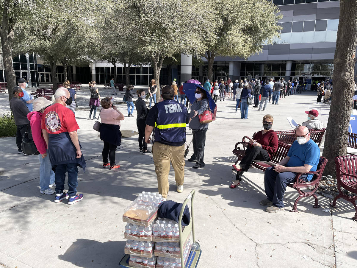 A worker hands out water to people in line for the second dose of the COVID-19 vaccine outside ...