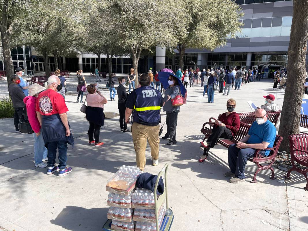 A worker hands out water to people in line for the second dose of the COVID-19 vaccine outside ...