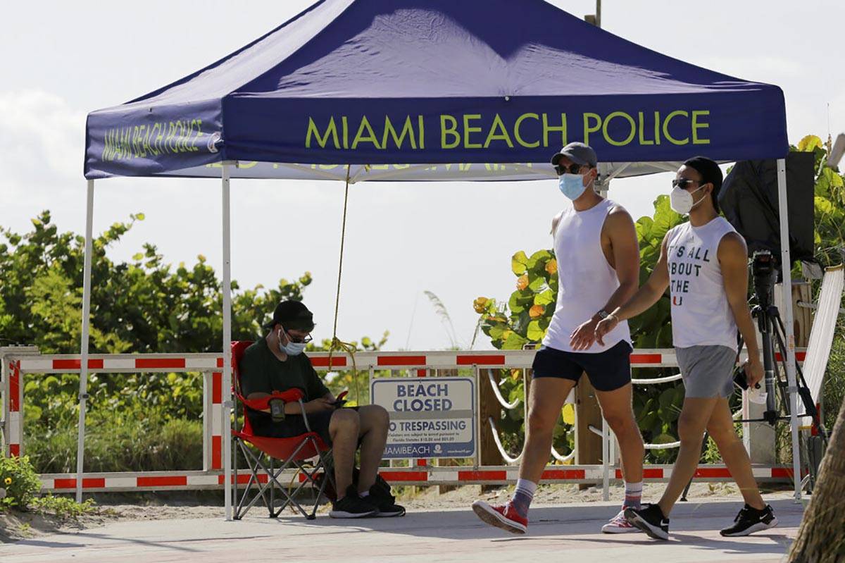 People wearing protective face masks walk past a closed entrance to the beach during the new co ...