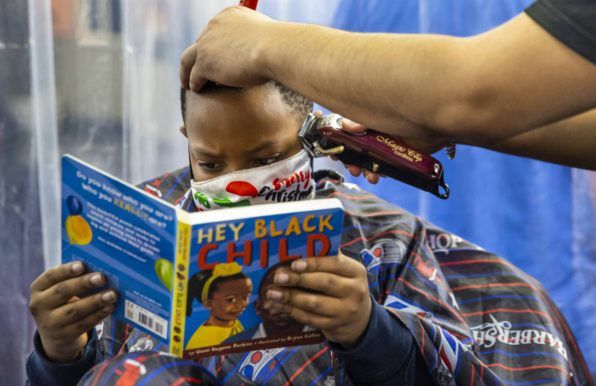 Earlvon Tate, 8, of Las Vegas, reads a book to student barber Jesus "Zeus" Magallon d ...