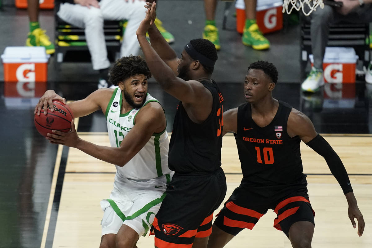 Oregon's LJ Figueroa (12) passes around Oregon State's Rodrigue Andela, center, and Warith Alat ...