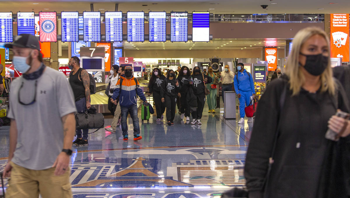 People move throughout baggage claim, wearing personal protective equipment to prevent the spre ...