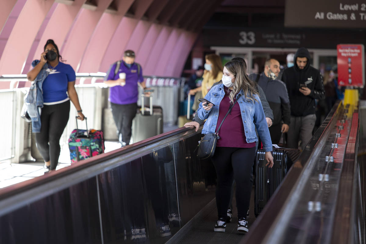 People exit McCarran International Airport, wearing personal protective equipment to prevent th ...