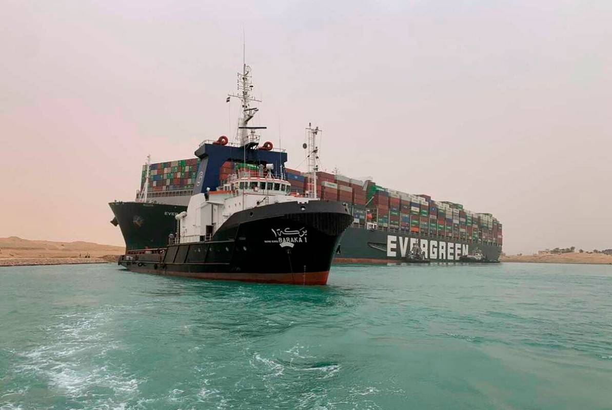 In this photo released by the Suez Canal Authority, a boat navigates in front of a massive carg ...