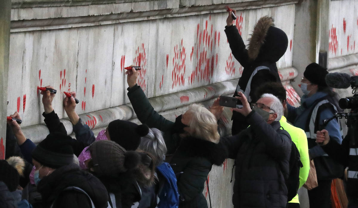 People paint red hearts onto the COVID-19 Memorial Wall mourning those who have died, opposite ...