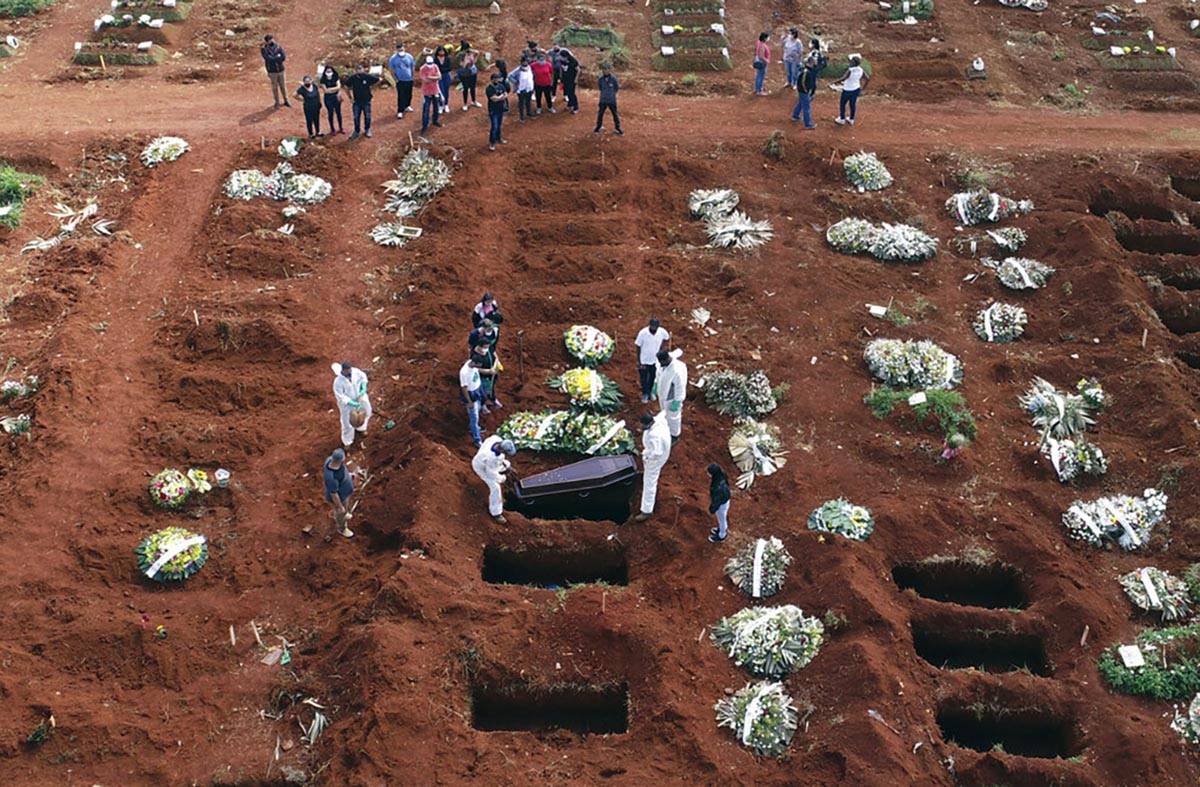 In this April 7, 2021, file photo, cemetery workers wearing protective gear lower the coffin of ...