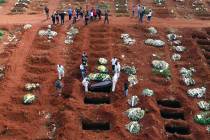 In this April 7, 2021, file photo, cemetery workers wearing protective gear lower the coffin of ...