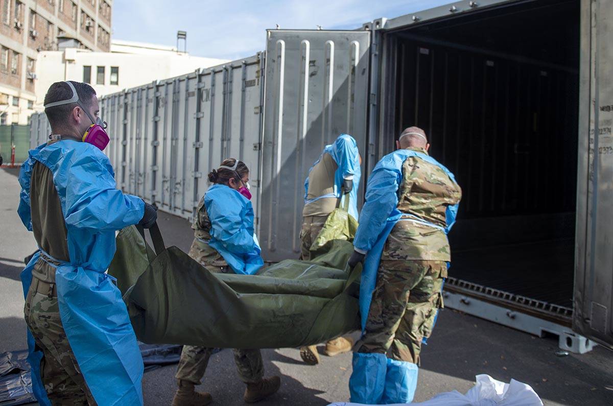 National Guard members, assisting with processing COVID-19 deaths, place bodies into temporary ...