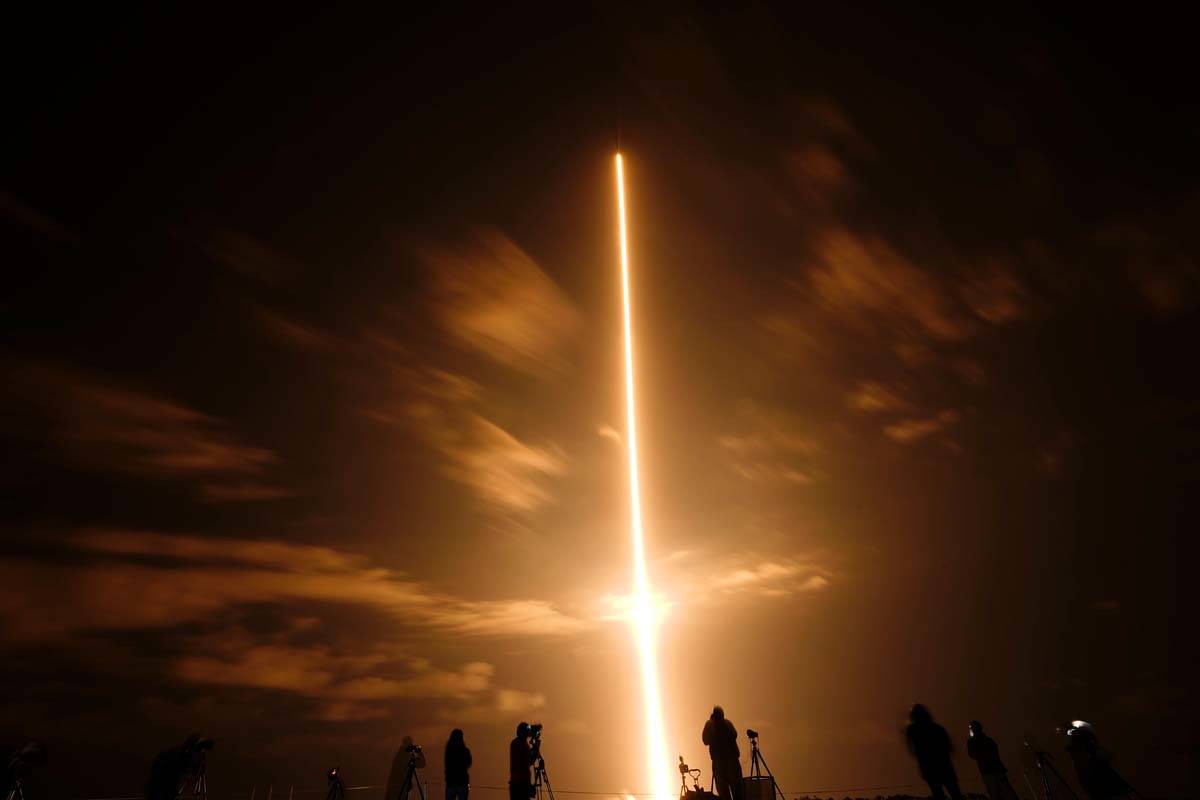 In this long exposure photo, photographers watch a SpaceX Falcon 9 rocket with the Crew Dragon ...