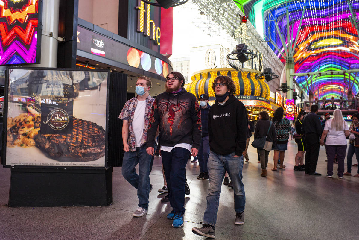 People, some wearing masks and others not, walk around the Fremont Street Experience in downtow ...