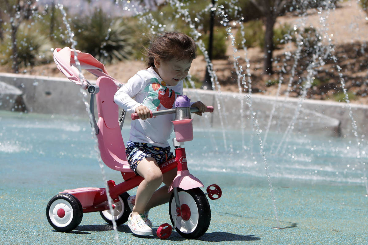 Luna Gyes, 2, of Summerlin rides a tricycle through the splash pad at Paseos Park in Las Vegas ...