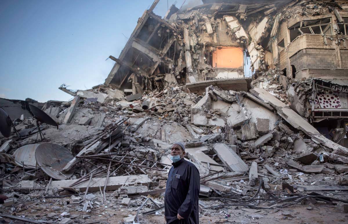 A Palestinian man looks at the destruction of a building hit by Israeli airstrikes in Gaza City ...