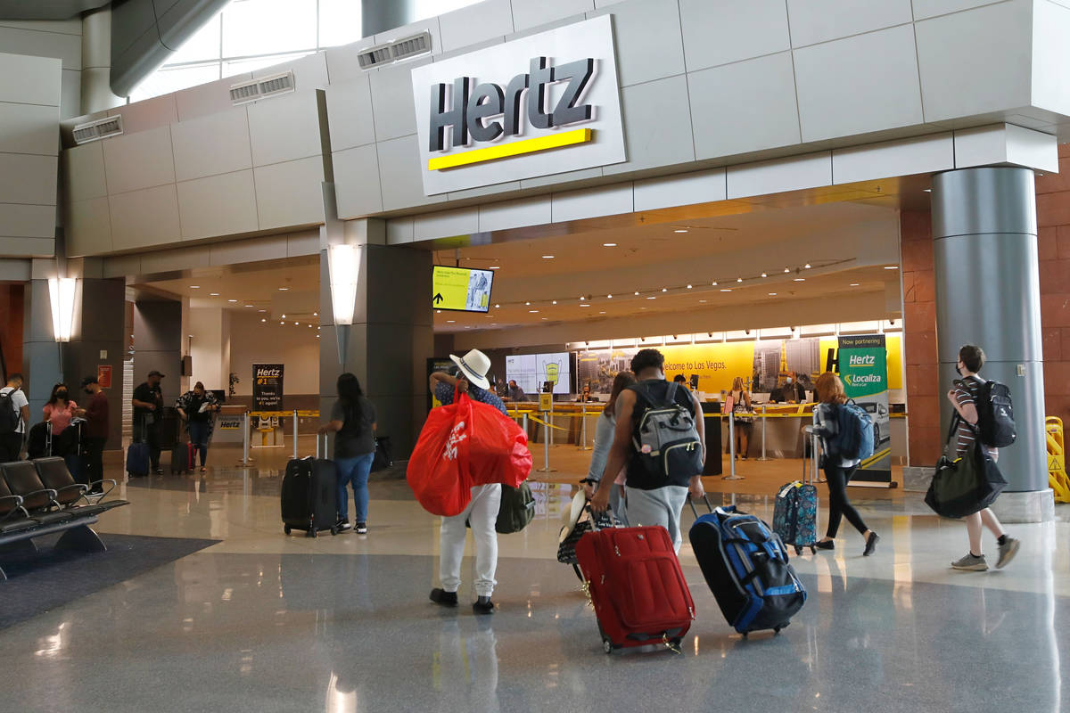 Travelers walk by a Hertz car rental at the McCarran Rent-A-Car Center in Las Vegas, Tuesday, M ...