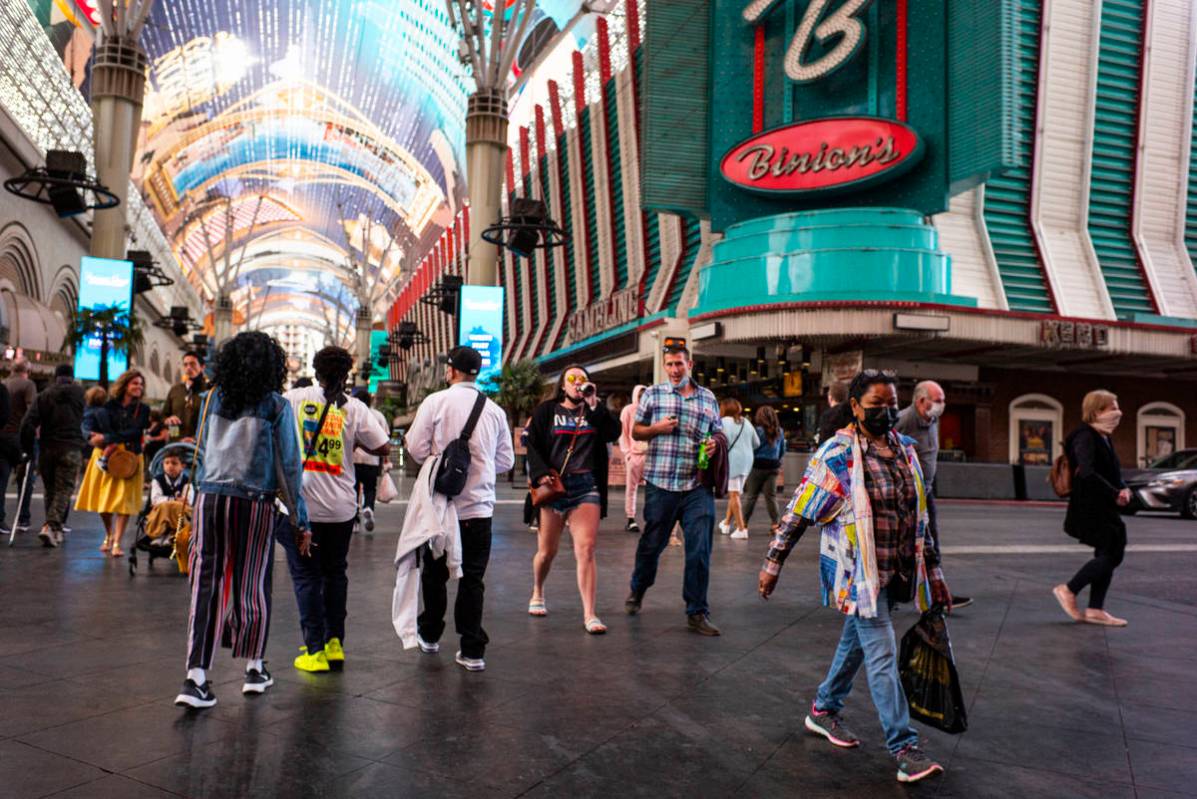 People, some wearing masks and others not, walk around the Fremont Street Experience in downtow ...