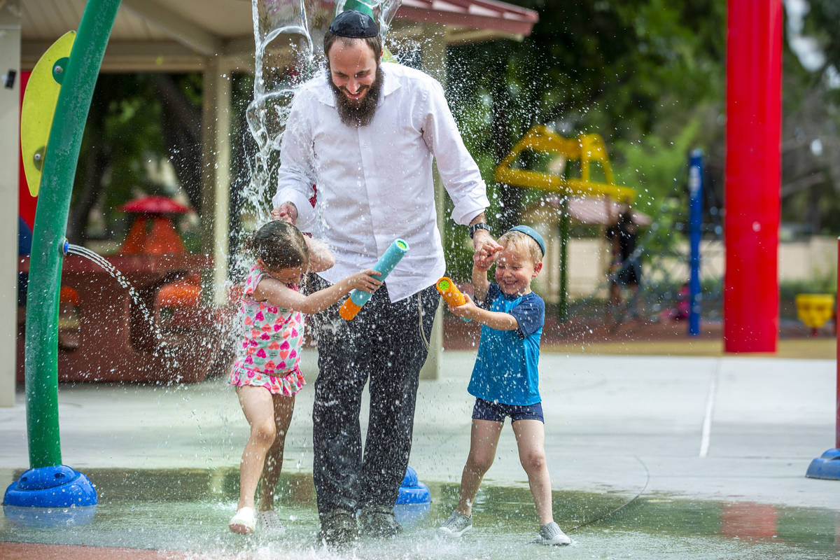 Rabbi Motti Harlig with his children Rivka, 5 , left, and Mendel, 3 right, get doused with wate ...