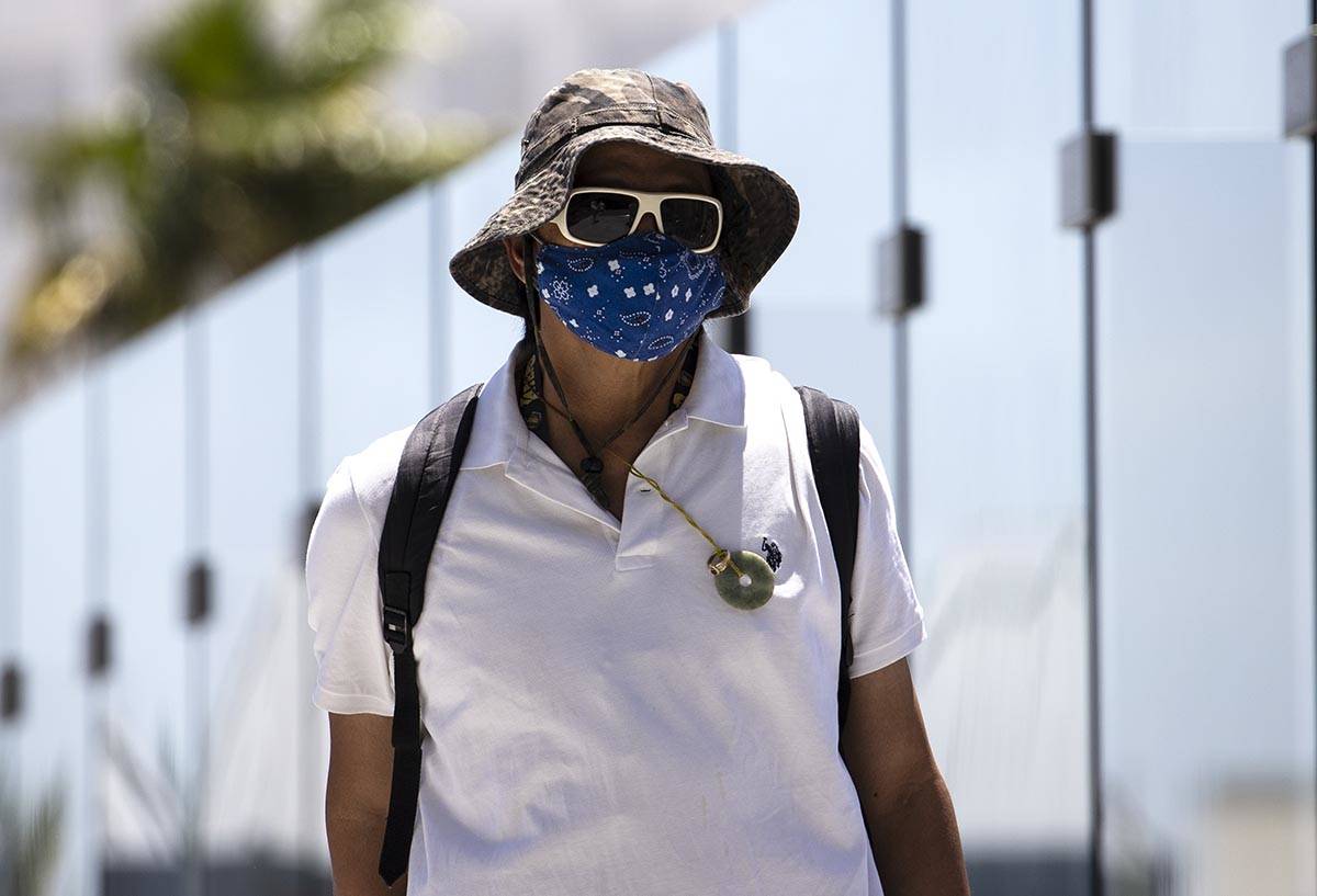 A pedestrian wears a large hat to protect himself from sun as he crosses the pedestrian bridge ...